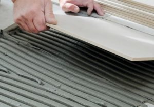 Hands-laying tiles with spacers on mortar for tile installation.