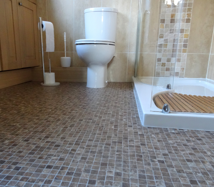 A well-appointed bathroom featuring intricate mosaic tile flooring in neutral tones, complementing the beige wall tiles and wooden cabinetry.