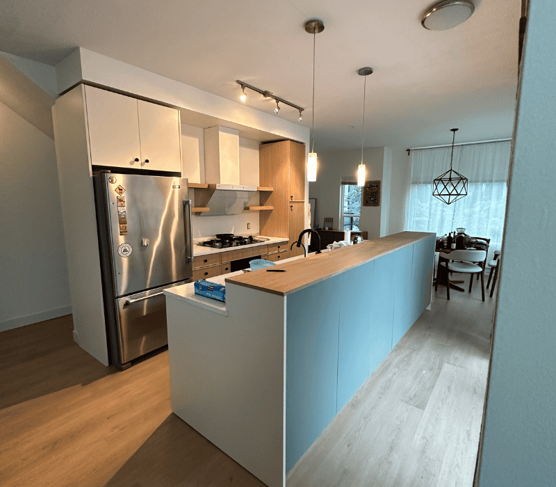 Modern kitchen with newly installed laminate flooring, featuring light blue cabinetry, stainless steel appliances, and wooden accents.