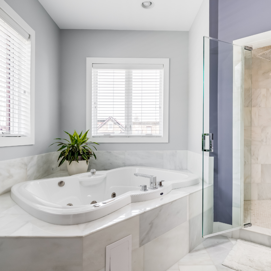 Corner bathtub in a bright bathroom with marble tiles and natural light, showcasing types of bathtubs