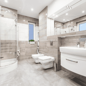 Modern bathroom with beige tiles, glass shower, and white fixtures including a bidet and floating vanity