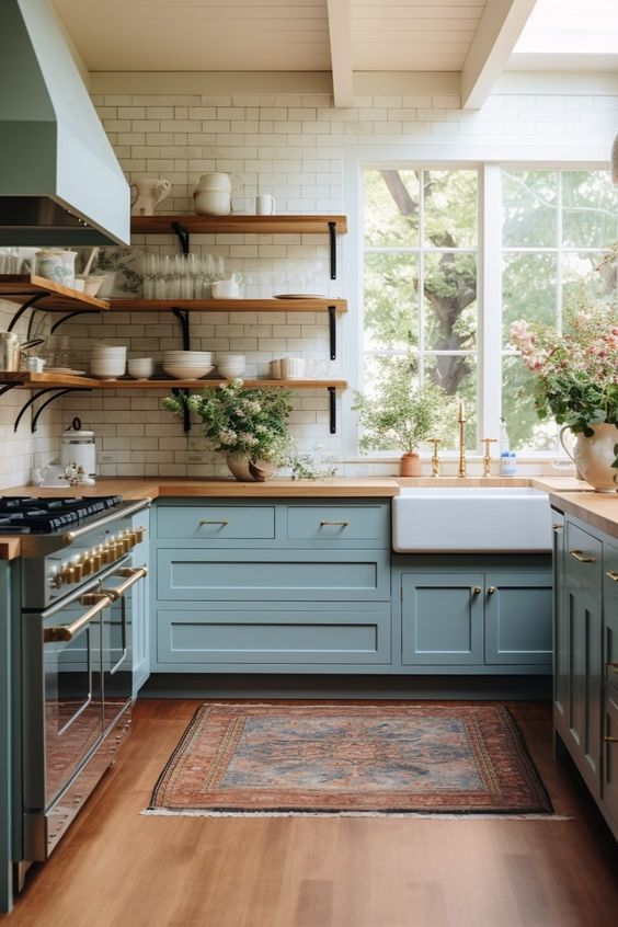 Charming kitchen style 2024 with pastel blue cabinets, open wooden shelves, farmhouse sink, and large windows.
