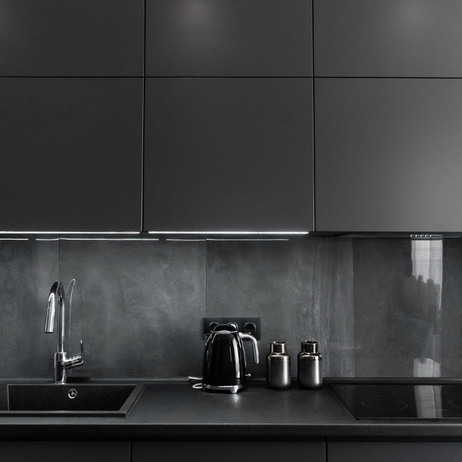 "Modern kitchen with black countertops, matching black backsplash, sleek cabinets, and a stainless steel faucet.