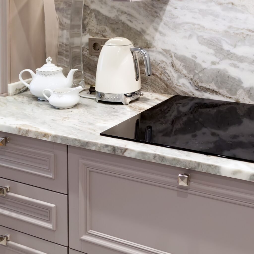 Elegant kitchen with light marble countertops, matching backsplash, and cream cabinets featuring a modern stovetop.