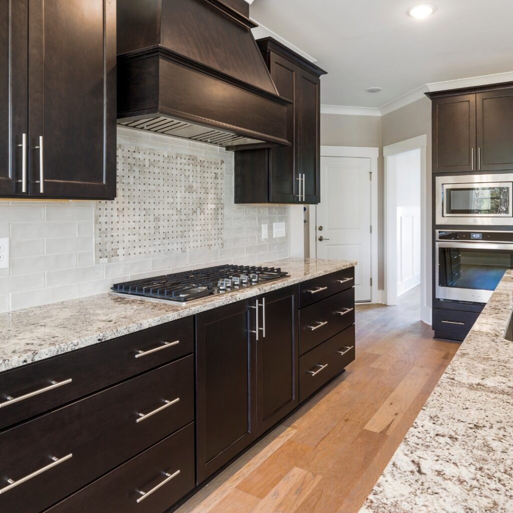 Quartz countertops and backsplash: Contemporary kitchen with dark wood cabinets, granite countertops, and a mosaic tile backsplash in a bright space.