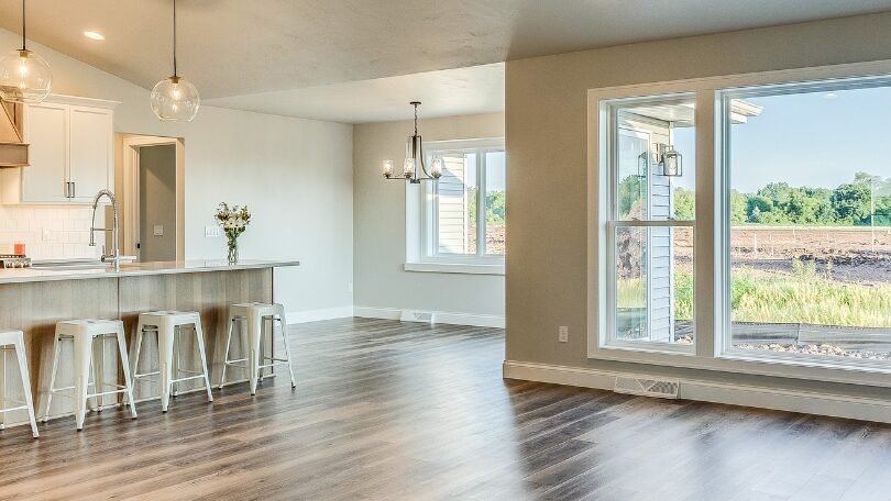 Open-concept kitchen with wood-look flooring, white cabinetry, and large windows.