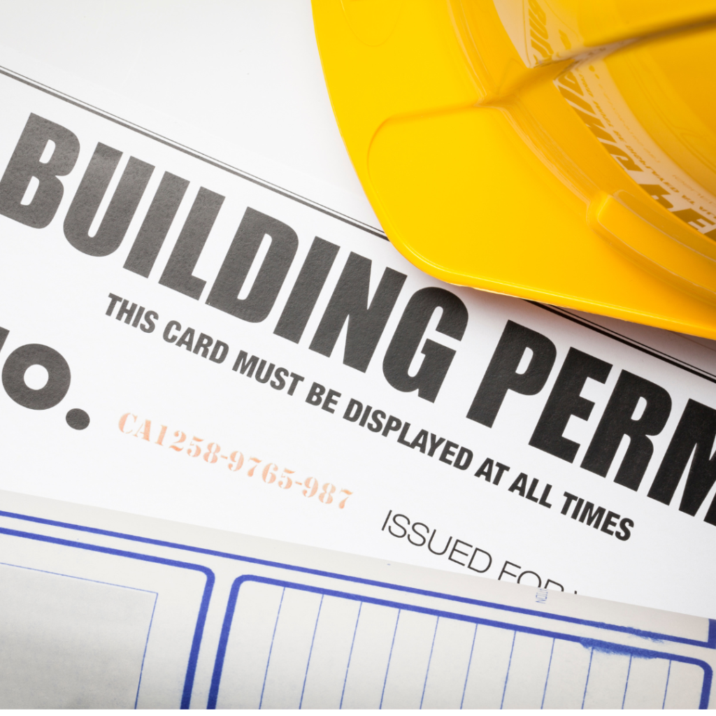 "Close-up of a building permit document with a yellow construction hard hat placed on top.