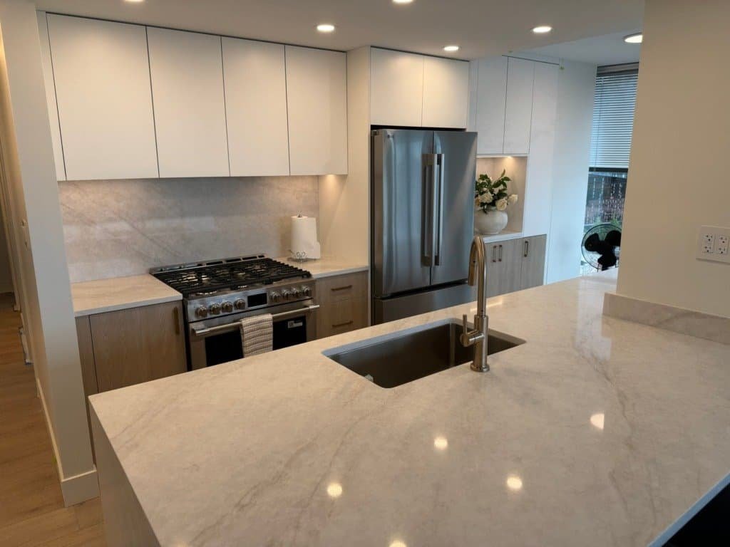 Downtown Vancouver condo kitchen with Taj Mahal quartzite waterfall island, full-height slab backsplash and undermount sink