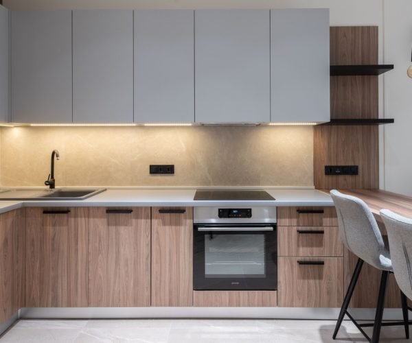 Modern kitchen with light wood cabinets, gray accents, minimalist countertops, and a subtle stone backsplash.